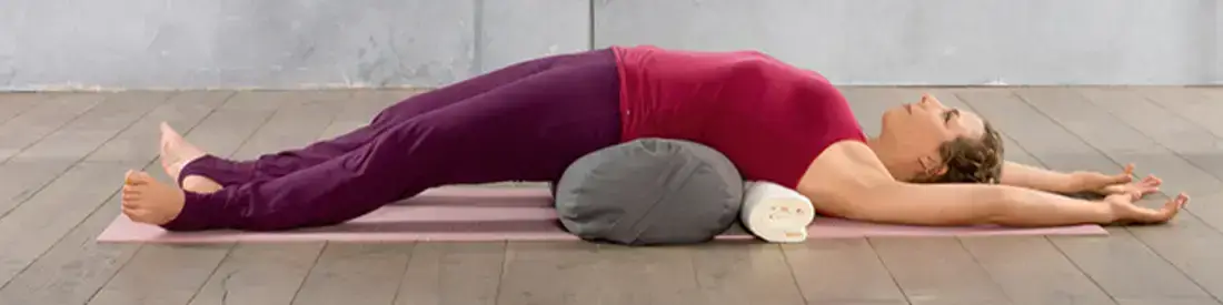 Yoga Teacher in a restorative backbend on a bolster.